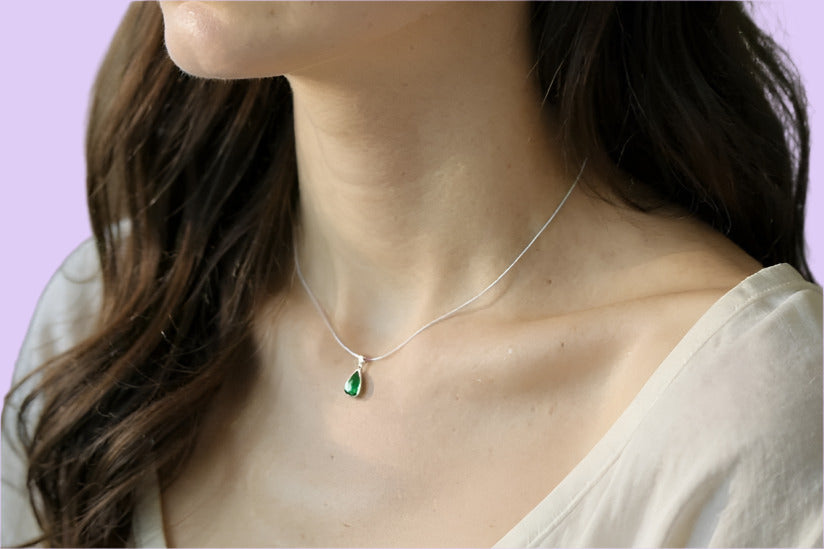 Woman wearing emerald green necklace and necklace against a neutral background